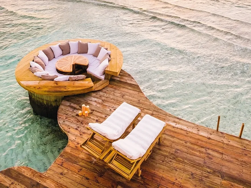 An overwater villa with a deck and steps down into a pale turquoise lagoon