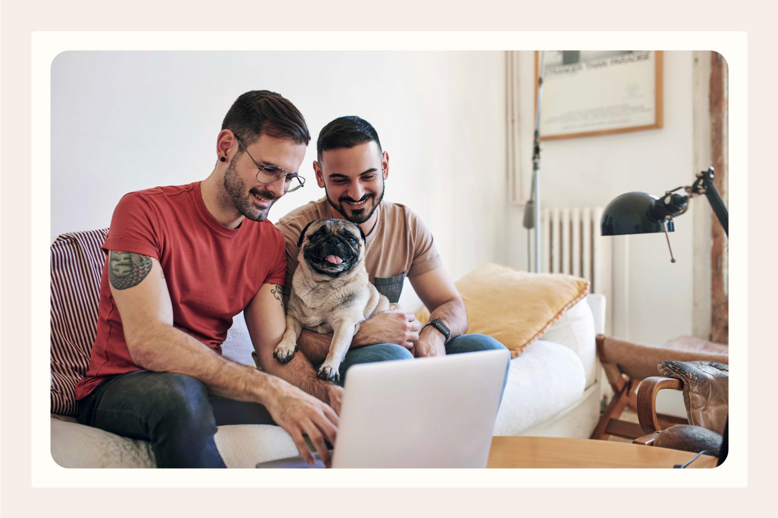 Two men holding a pug smile as they type on laptop