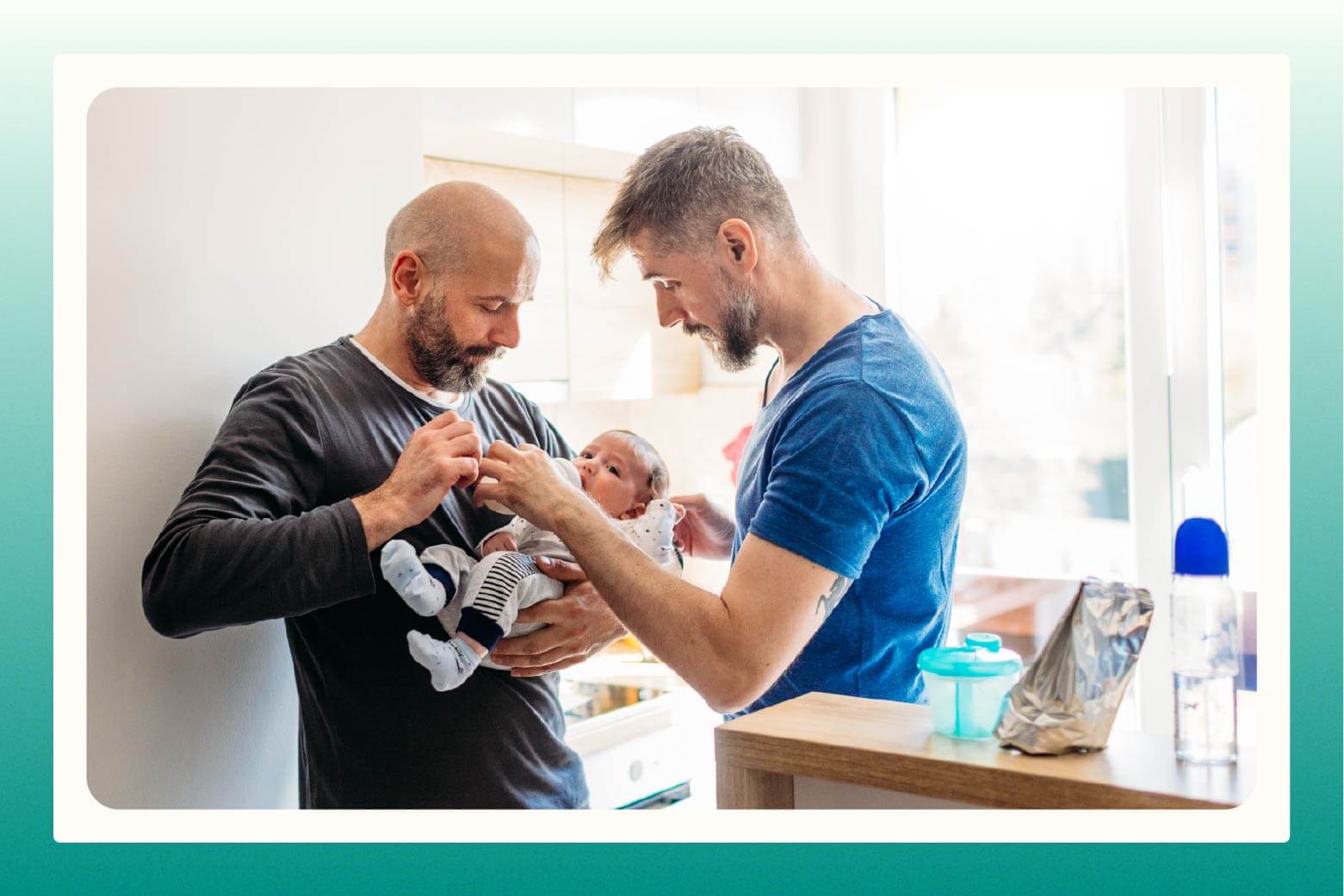 One man cradling baby in his arm while second man feeds the baby a bottle