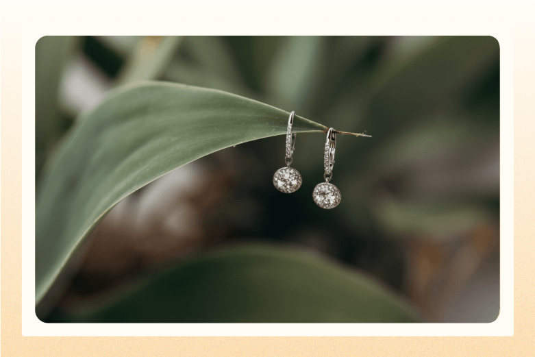 pair of diamond drop earrings hang from a green leaf