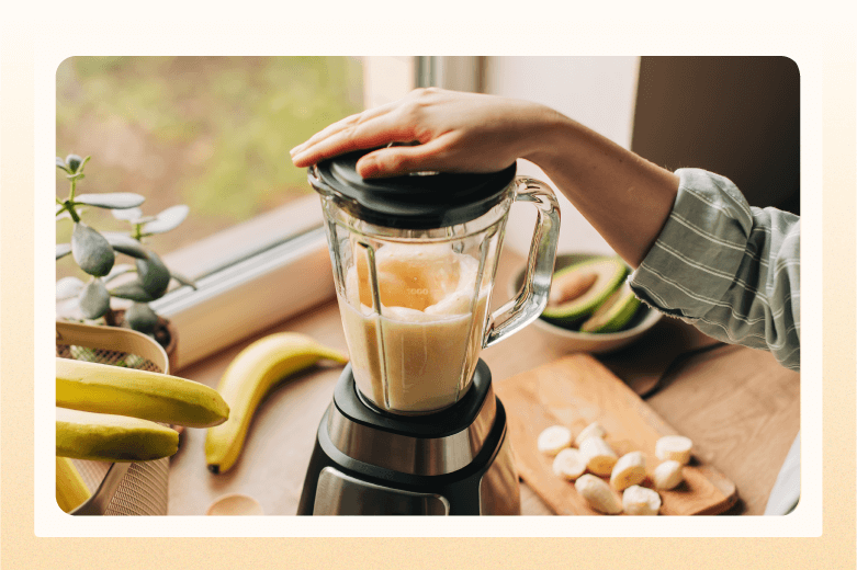 with bananas and avocados in background, a person's hand sits atop a whirring blender
