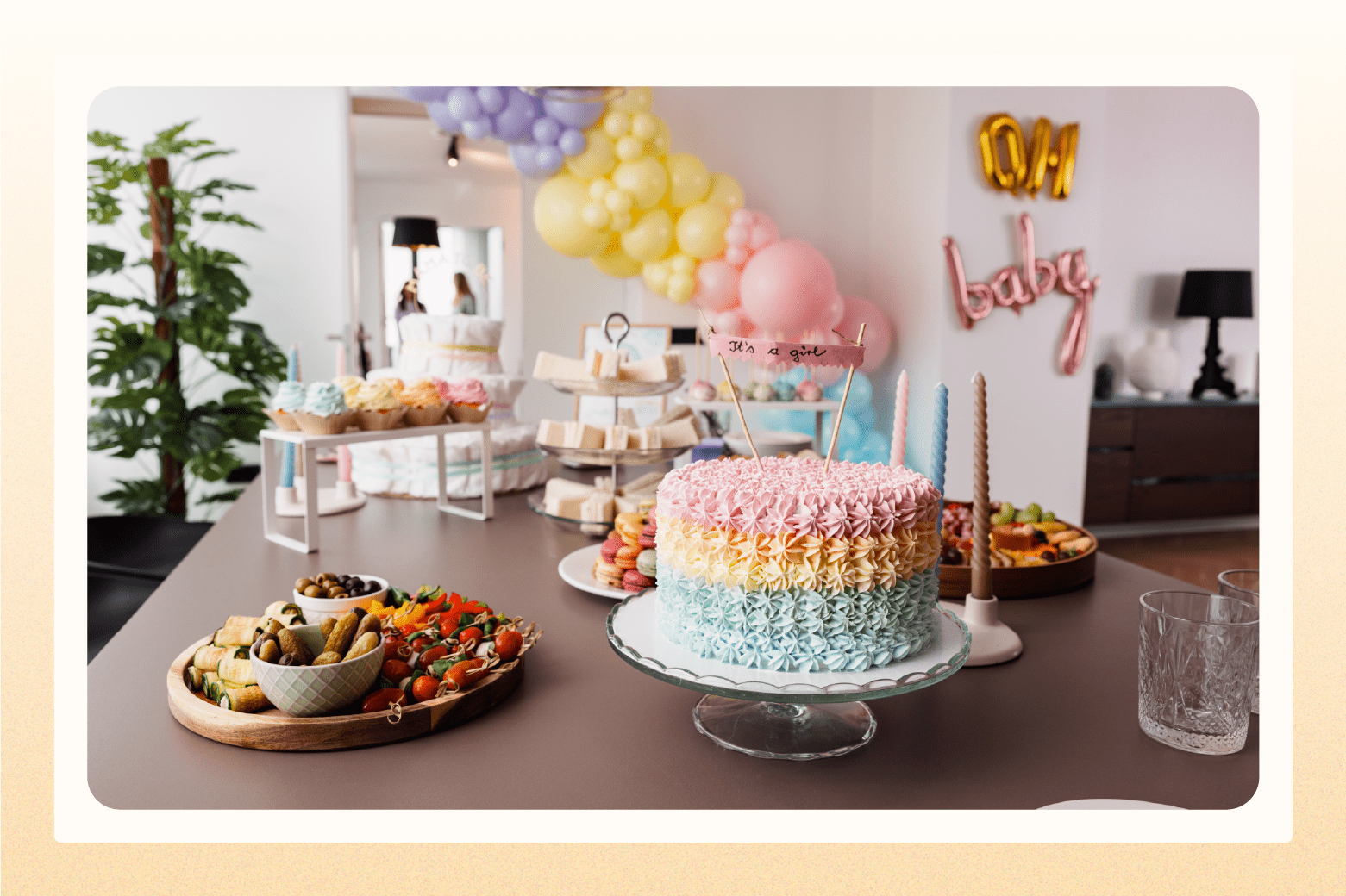 Baby sprinkle table with rainbow cake and balloons in background