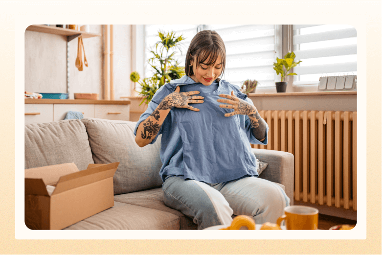 woman holding blue shirt up to her chest with open box next to her on sofa