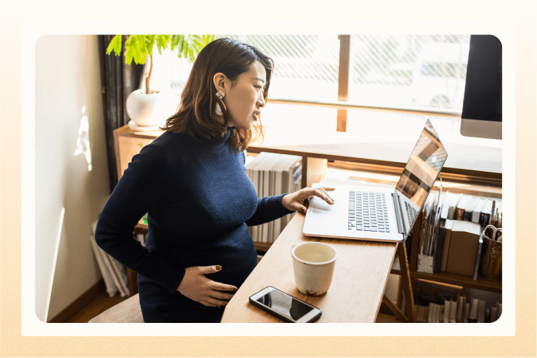 Pregnant woman sitting at desk with laptop and her hand on belly 