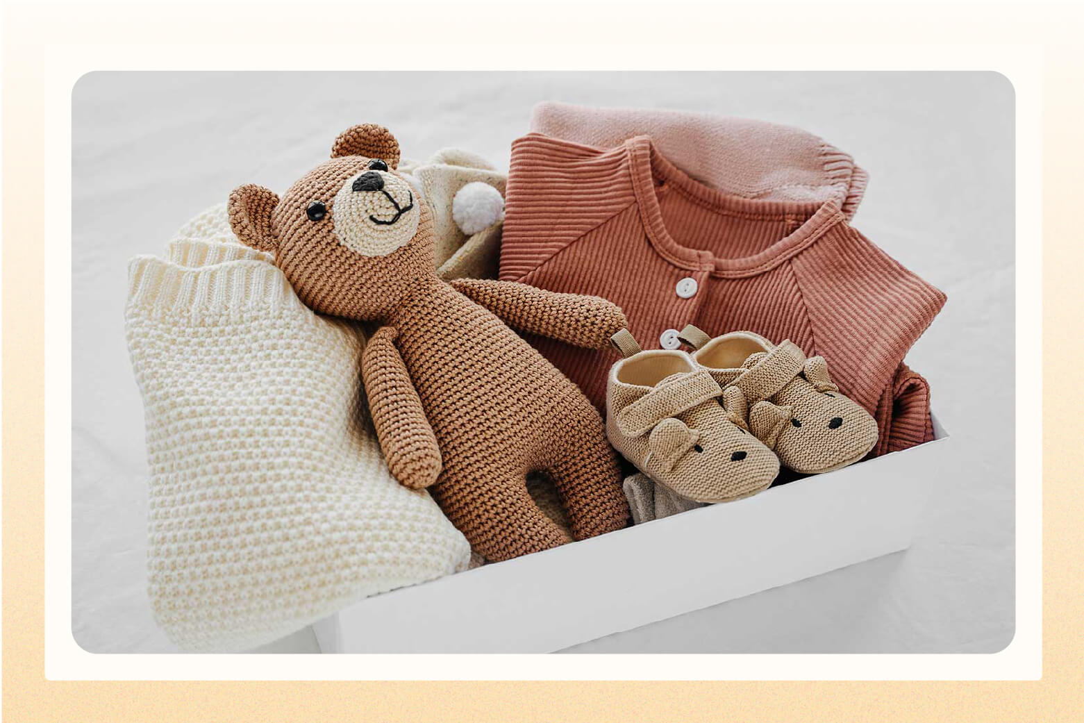 Box holding knitted baby clothes, tiny shoes, and a knitted teddy bear