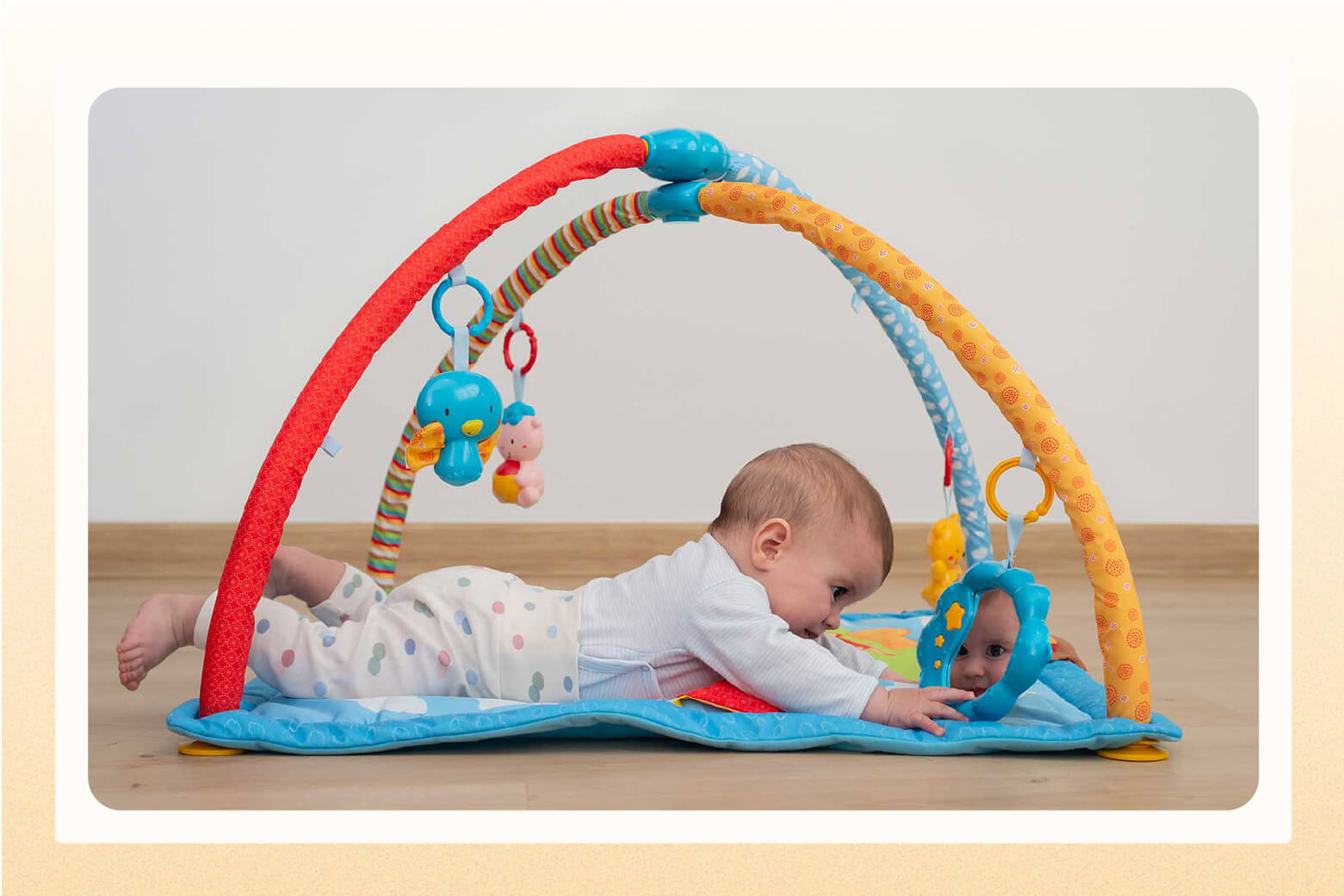 Baby laying on tummy on a playmat with colorful arcs above baby with toys dangling