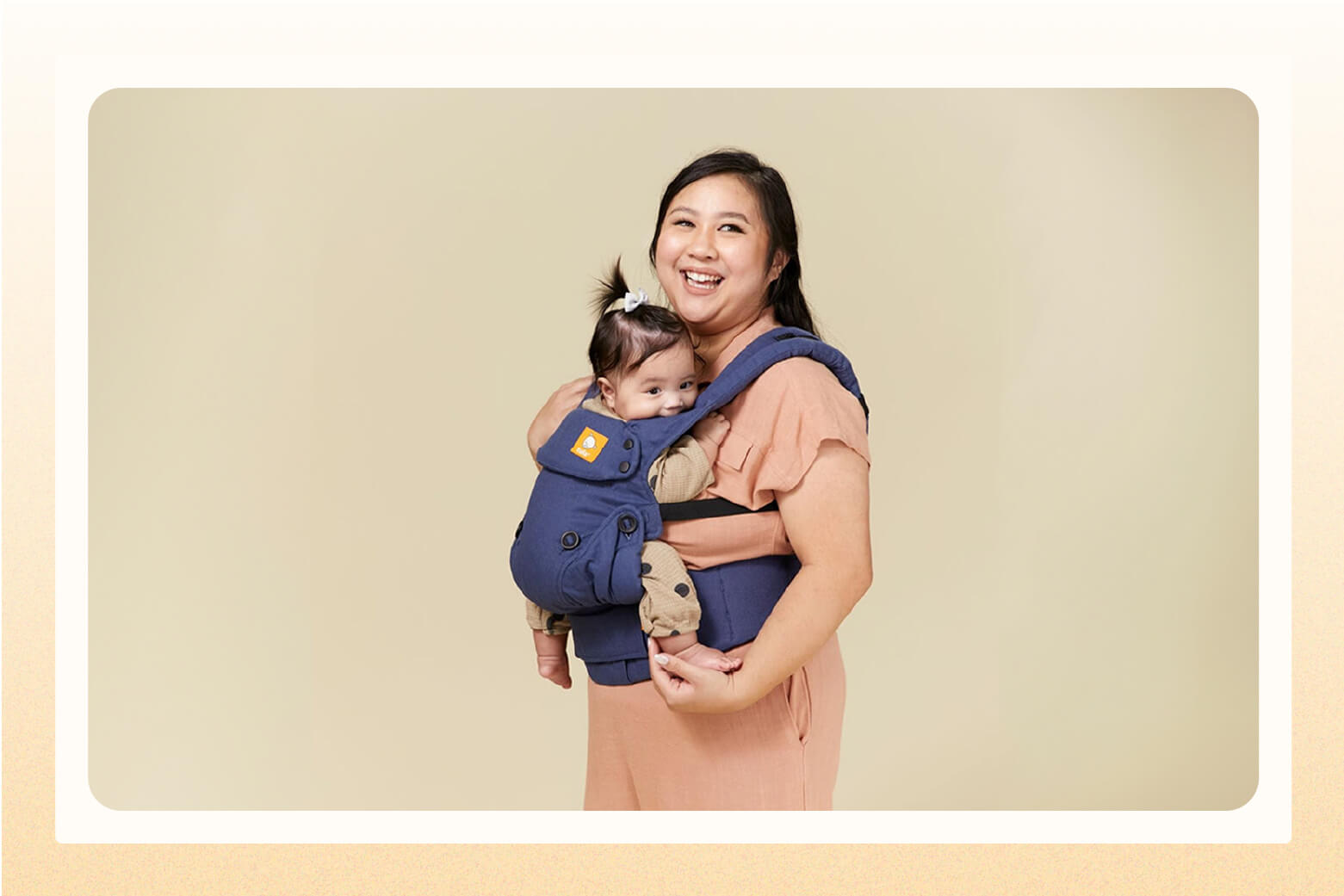 Smiling mom wearing a blue baby carrier on her chest with baby in it