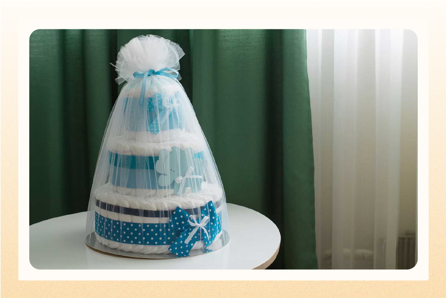 Three-tiered diaper cake wrapped in tulle with blue ribbons as accents