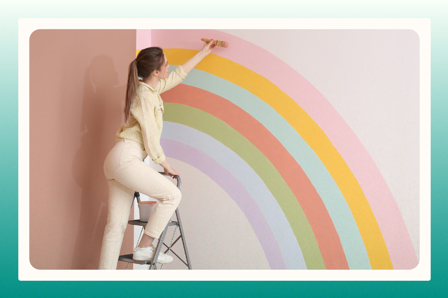 Woman on step ladder paints pastel mural on nursery wall
