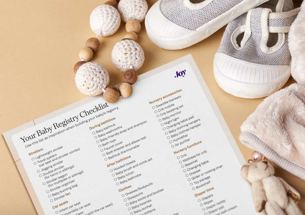 Partial view of Joy's printable baby registry checklist, with baby shoes, blanket, rattle, and tiny teddy bear alongside it
