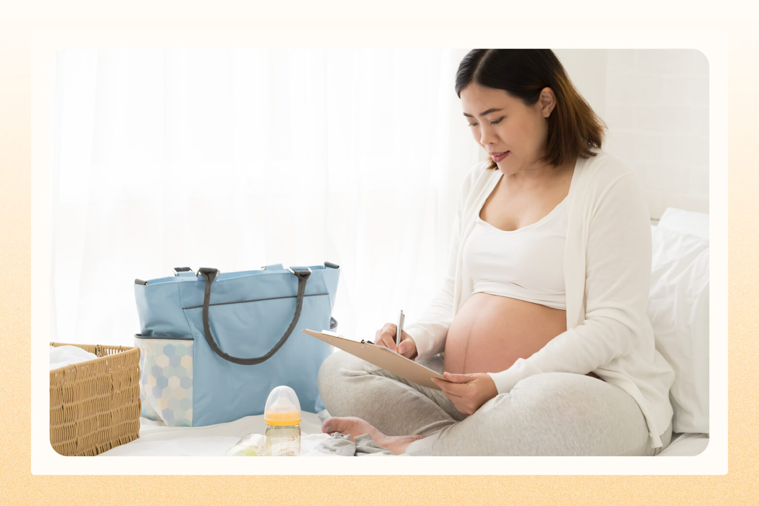 Pregnant mom working on a checklist next to a diaper bag and baby bottle