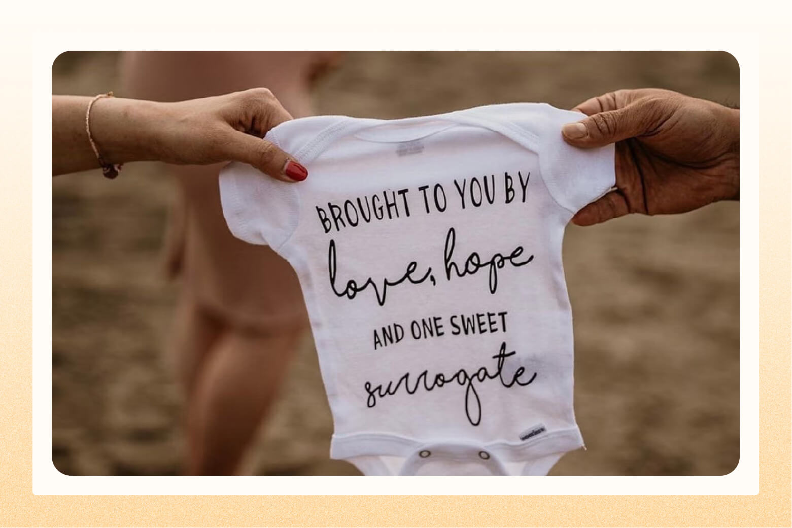 two hands holding up a white onesie that reads "brought to you by love, hope and one sweet surrogate"