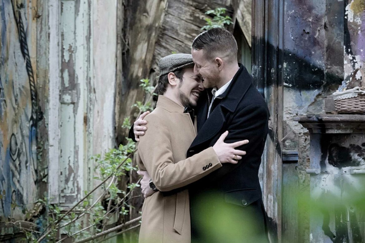 What to wear in engagement photos: Two men embracing wearing complementary peacoats in winter