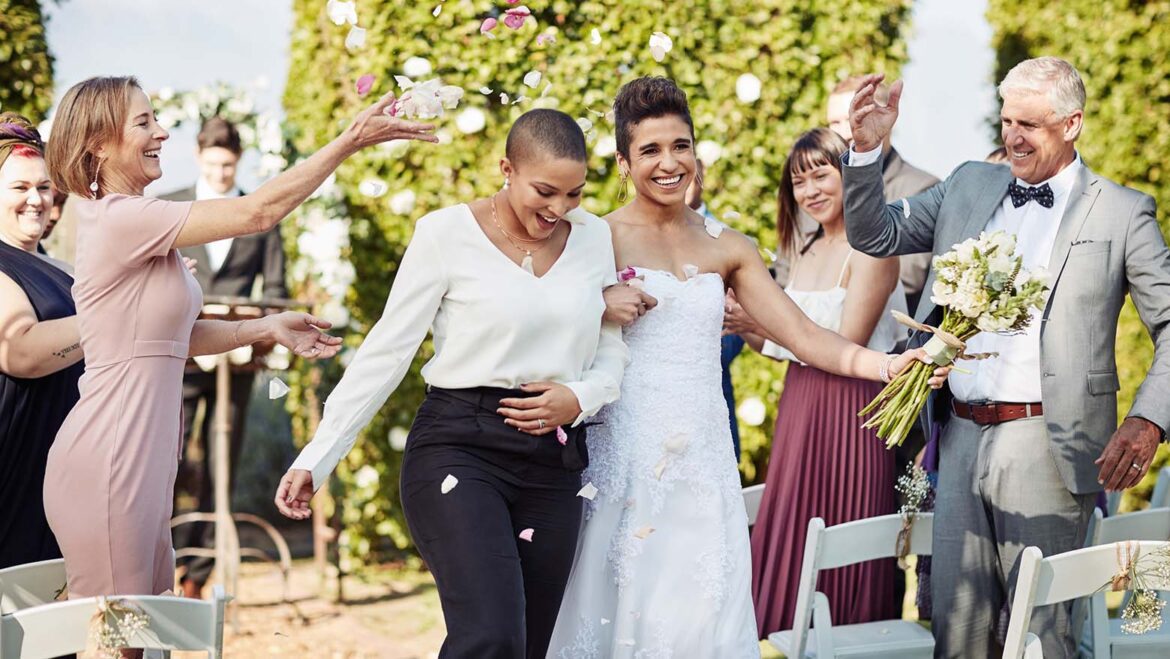 A couple leaving their wedding venue with their guests showering them with confetti.
