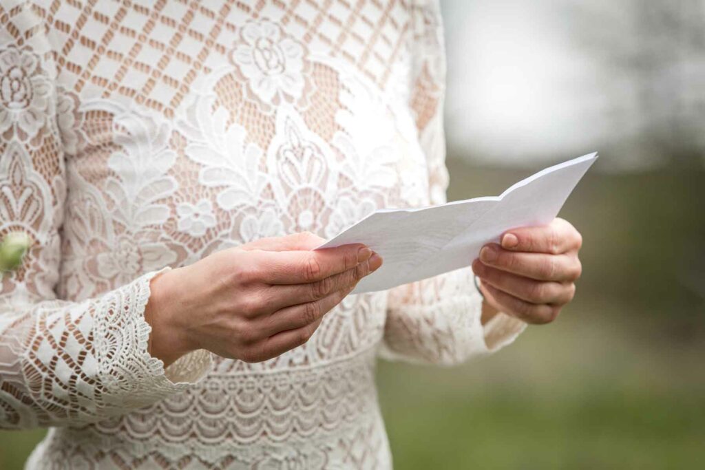 A woman in a lace wedding dress reading her wedding vows out loud