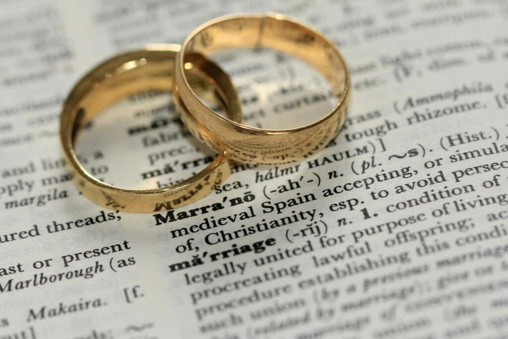 A pair of gold wedding bands on top of a dictionary entry for marriage
