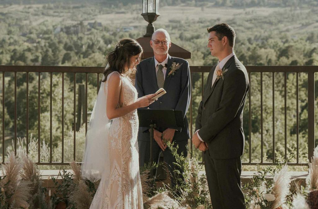 A woman in a wedding dress reading wedding vows to a man in a suit in front of an officiant