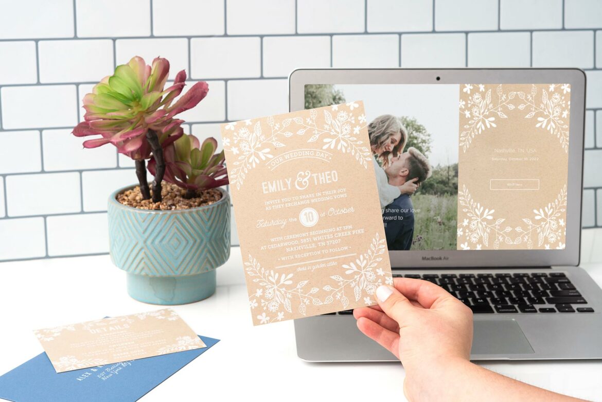 A hand holding up Joy's Rustic Floral wedding invitation in front of a laptop screen with a matching wedding website