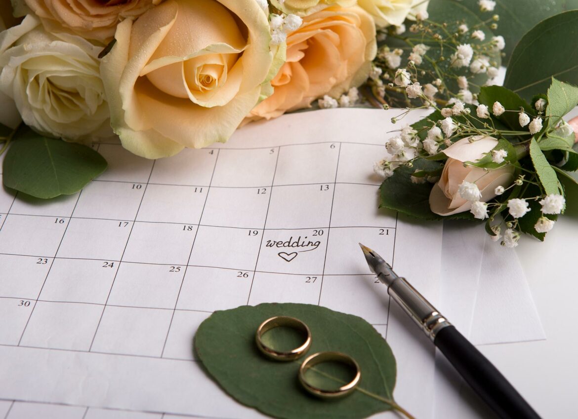 A calendar surrounded by roses with a wedding date indicated and two wedding rings below the date