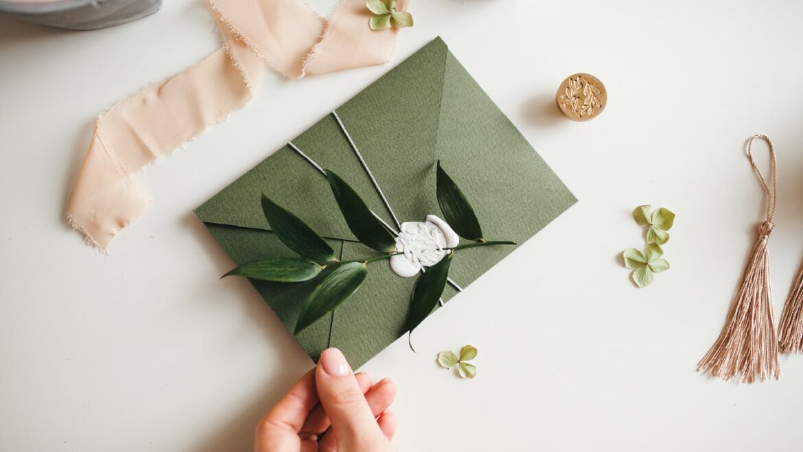 Green wedding invitation envelope with a leafy twig attached via a white wax seal