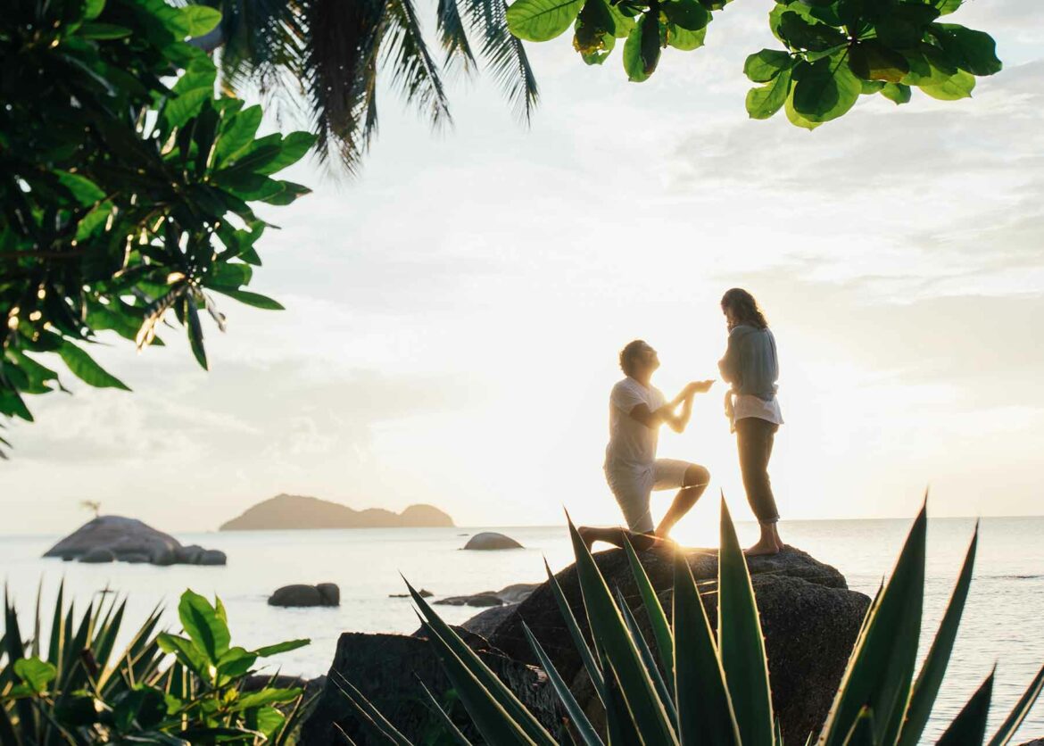 A simple proposal in a tropical destination with a couple standing on a rock with water in the background