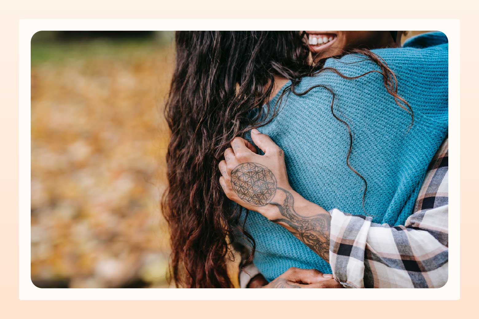 Cropped image showing only the back of one person and the tattooed arm and smile of another person as they embrace 