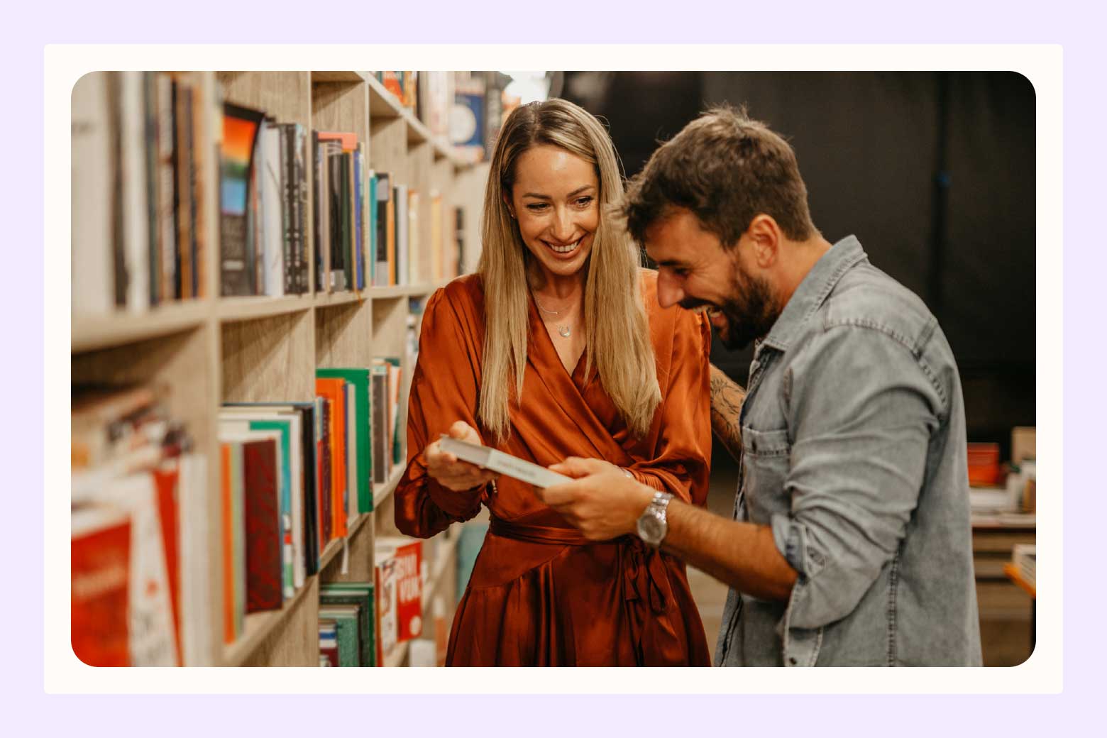 Couple laughs as woman shows her fiance a book while they're in a library