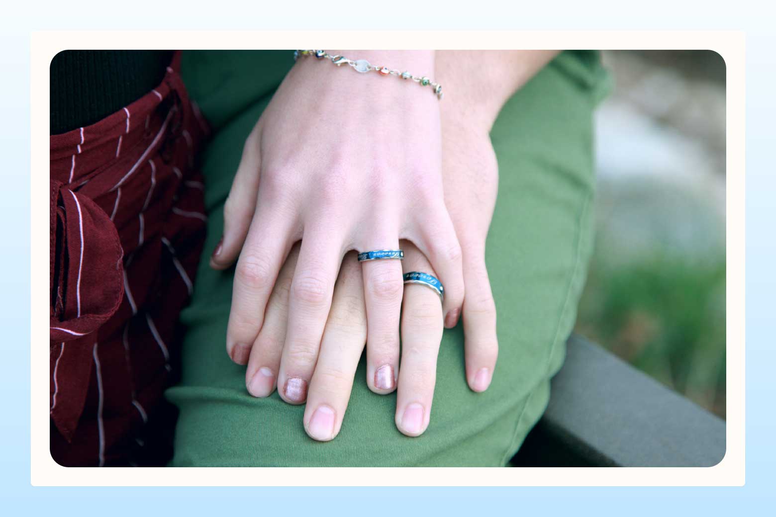 Close up of two hands, one resting atop the other, showing off matching engagement rings