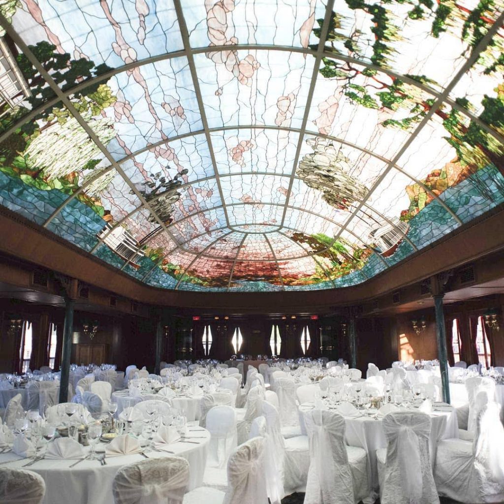 wedding reception setup with white chairs and tables under a stained-glass ceiling at the bahia resort hotel venue in san diego