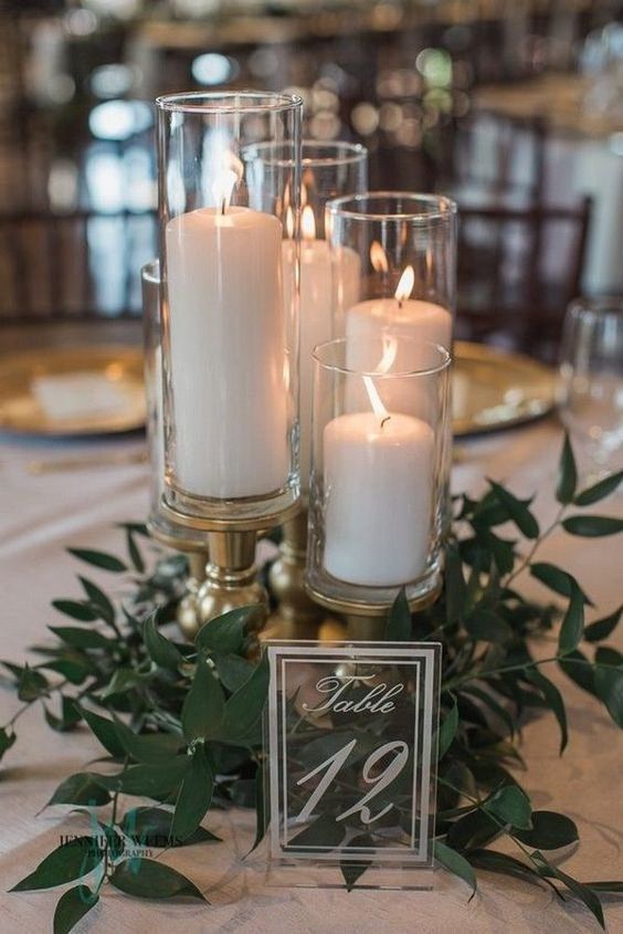 candles in clear candleholders and greenery arranged on a wedding reception table