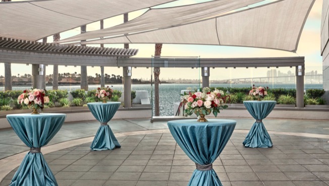 cocktail hour setup with small blue tables and flowers at the sunset terrace at lowes coronado bay resort in san diego