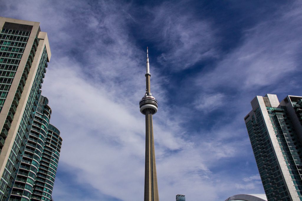 view of the cn tower in toronto under a blue, cloudy sky with surrounding buildings
