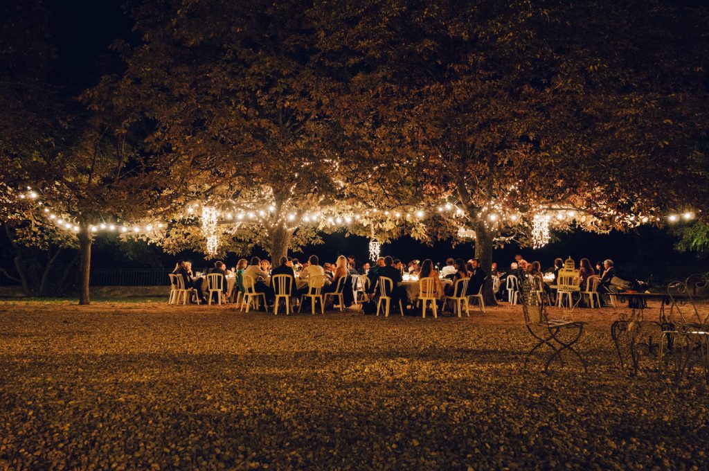 people gathered at outdoor wedding dinner next to lighted up trees