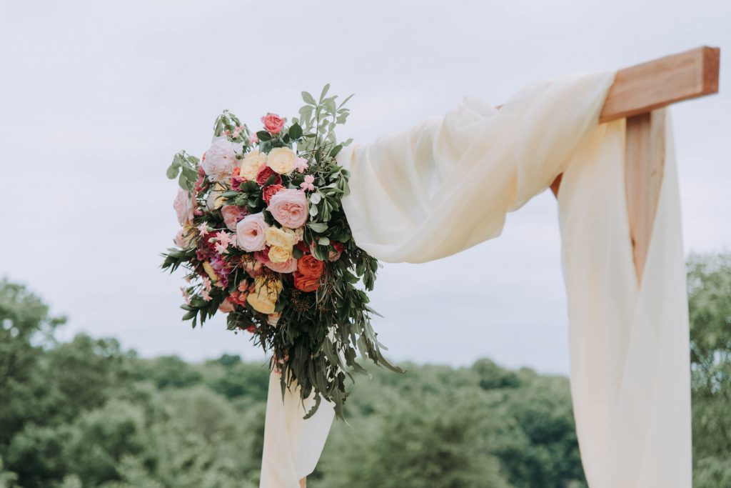 wedding ceremony arch with white fabric and bouquet of flowers