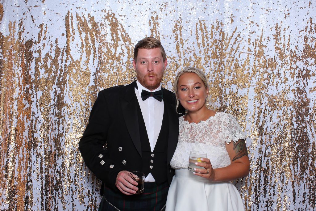 married couple stand in front of customized gold photo booth for a photo