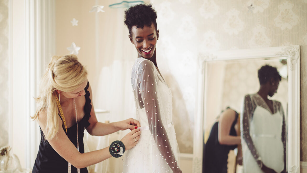 designer assisting woman with wedding dress fitting