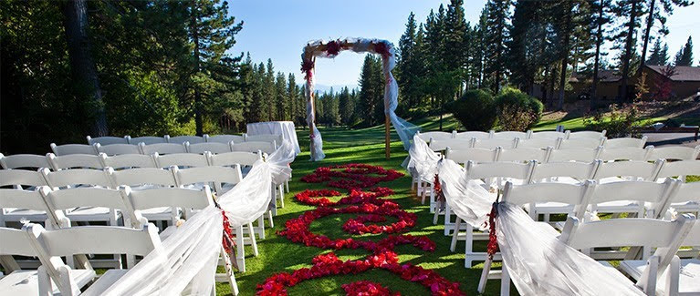 white chairs, an arch, and a rose-petal-covered aisle set up for a wedding on the golf course at the chateau at incline village