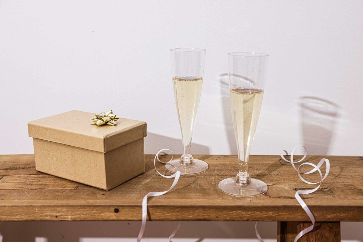 Wooden table topped with a brown wedding gift box and two filled champagne flutes.