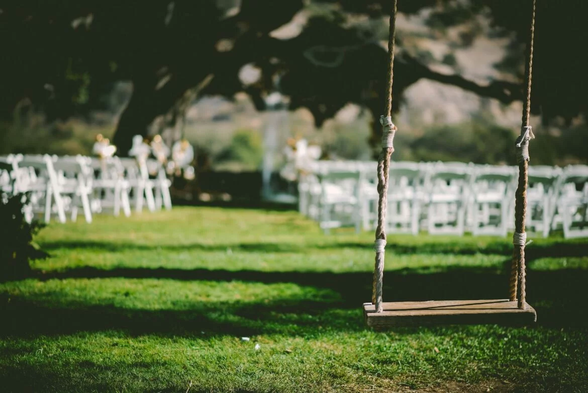A wooden swing hanging in front of the set-up for an outdoor wedding ceremony