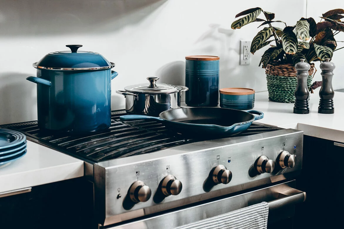 Blue cast iron cookware, including a skillet and stockpot, and a stainless steel saucepan on a kitchen stove
