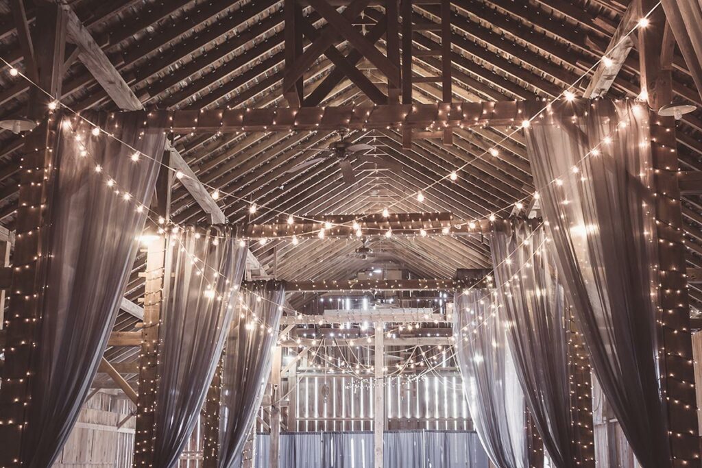 Strands of wedding lights draped with fabric in a rustic venue