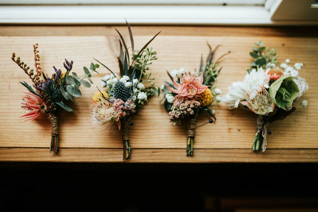 Four wedding boutonnieres wrapped with twine on a wood table