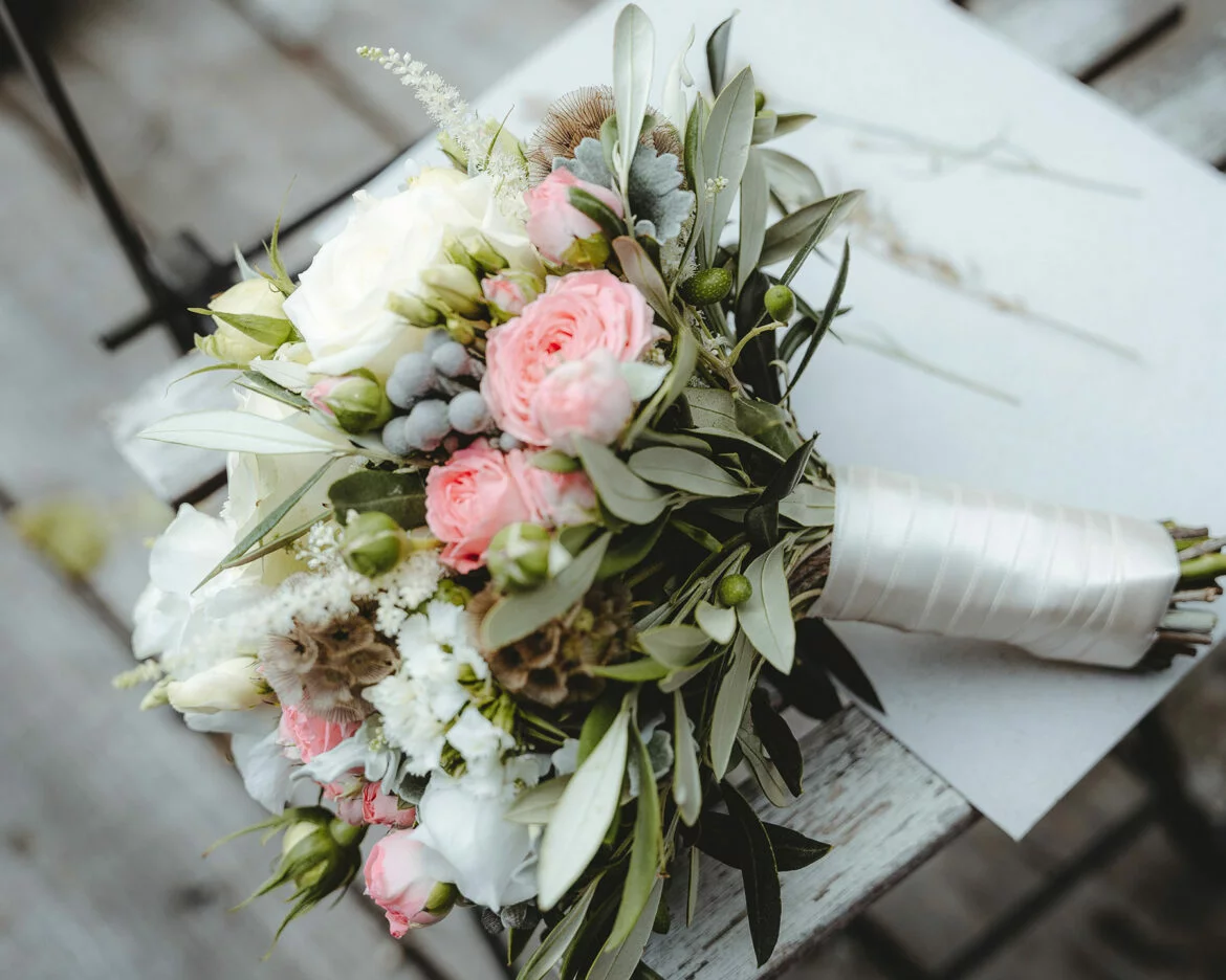 Closeup of a wedding bouquet with white and pink flowers and greenery fillers wrapped with a satin ribbon
