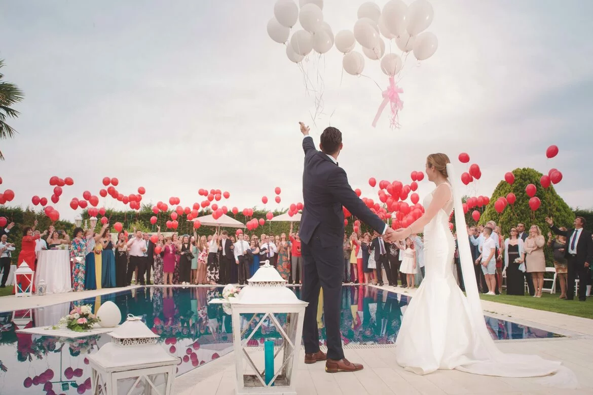 A couple dressed in wedding attire does a balloon release with their guests