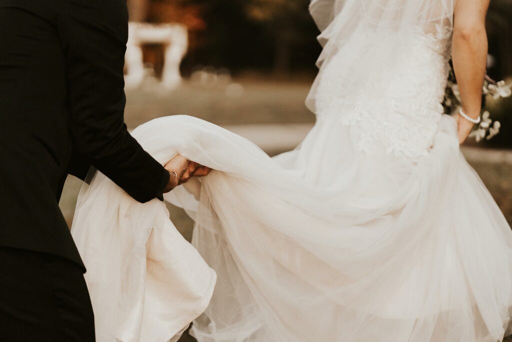 A person in a black suit holding the train of a wedding dress