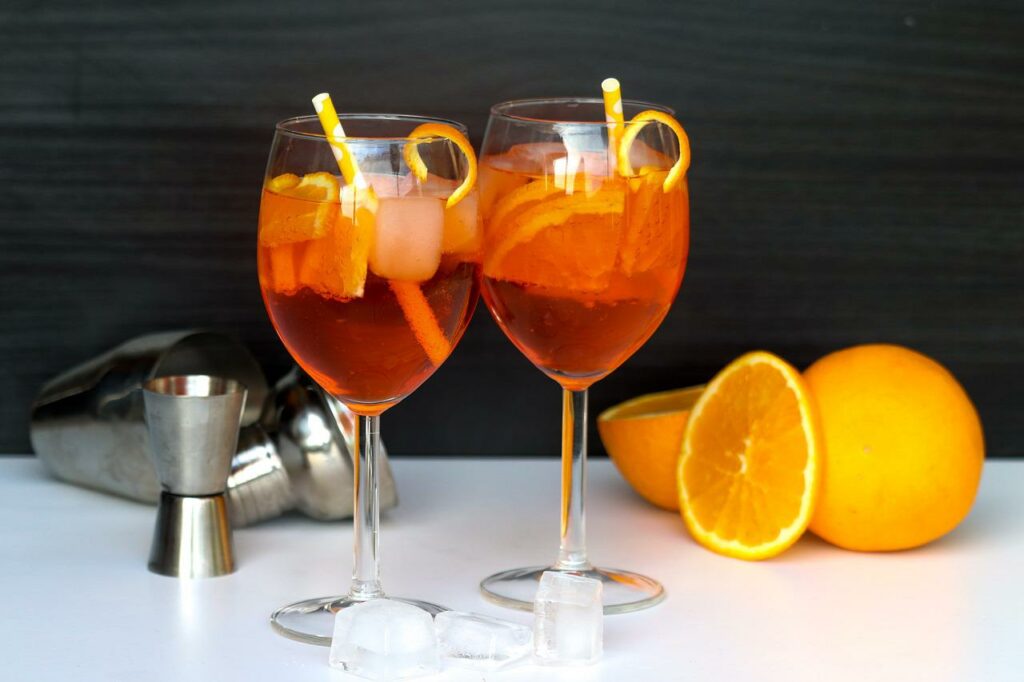 Two Aperol Spritz drinks next to oranges and mixer