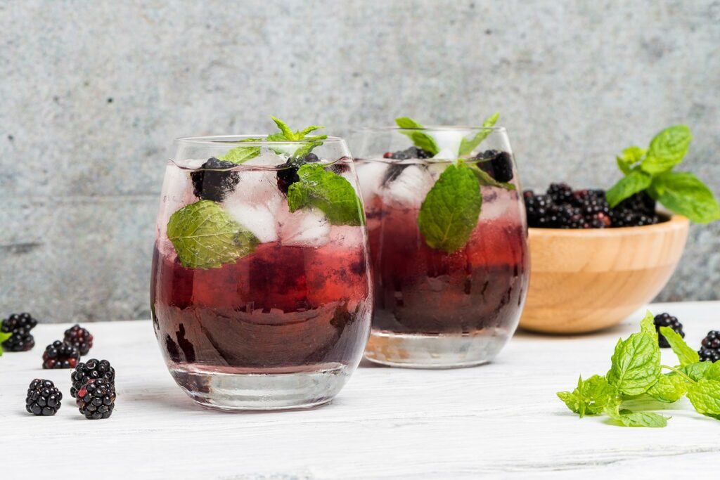 Two glasses of blackberry beverage garnished with mint leaves