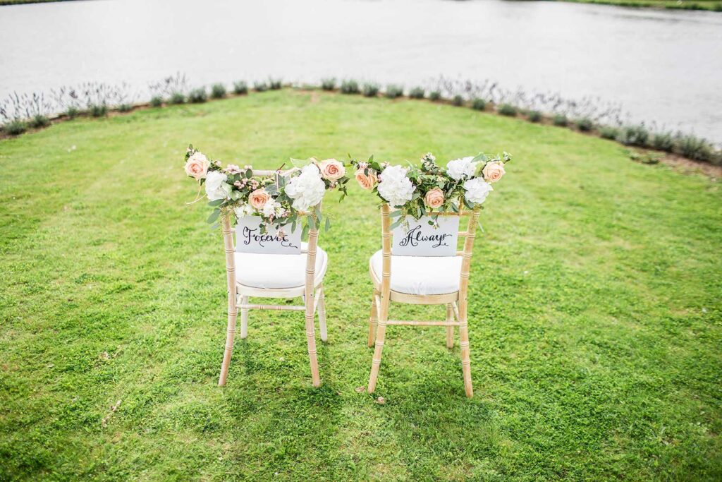 Two chairs on a green lawn adorned with flowers and signs that read forever and always