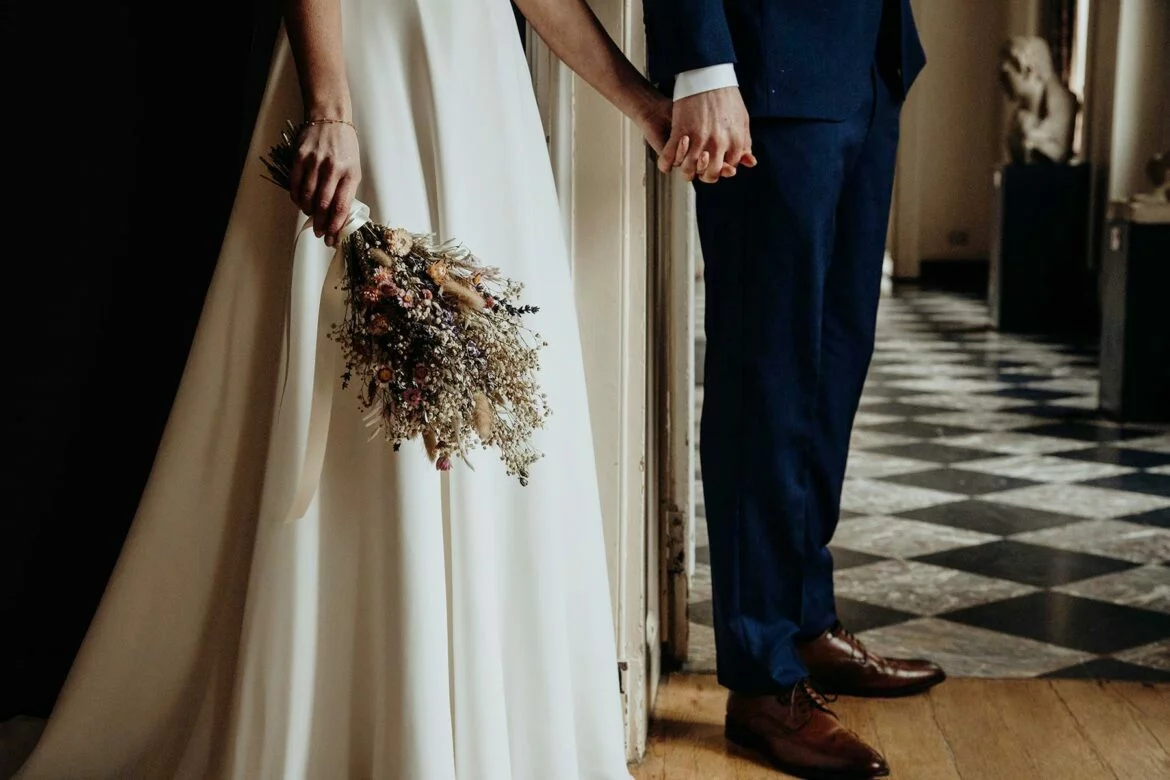 Couple in wedding attire holding hands and a bouquet of dried flowers
