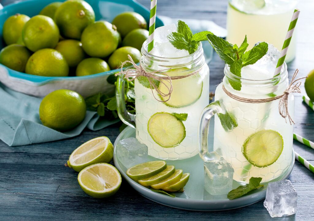 Pitcher of vodka mint limeade with two mason jars and a bowl of limes